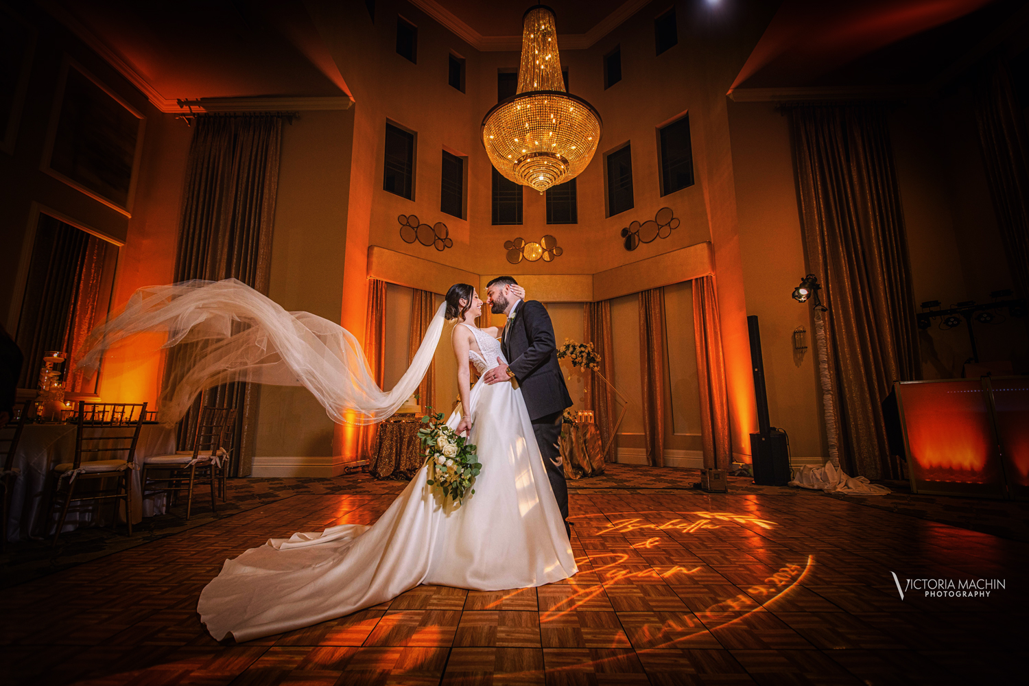 Stunning luxury wedding at Parkland Country Club, where the newlyweds share a romantic moment under a breathtaking chandelier. The bride's flowing veil and warm golden ambiance create a fairytale scene, beautifully orchestrated by Zeta Event Productions, a full-service Miami wedding planning and event design company. Captured by Victoria Machin Photography, this elegant South Florida wedding is a dream come true.