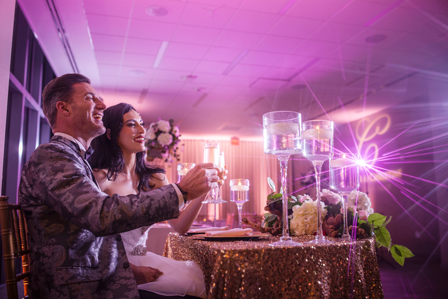Bride and groom toasting with champagne at their Miami wedding reception, surrounded by candlelight, floral décor, and purple uplighting by Zeta Event Productions.