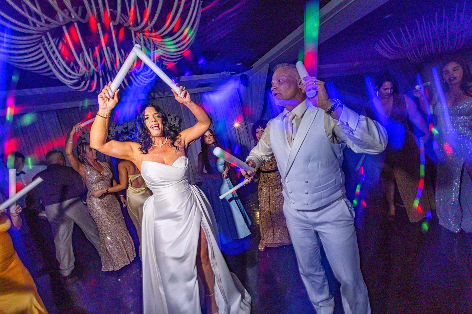 Bride and groom dancing with LED foam sticks during La Hora Loca at Brisas On The Bay, lit by colorful DJ lighting effects by Zeta Event Productions.