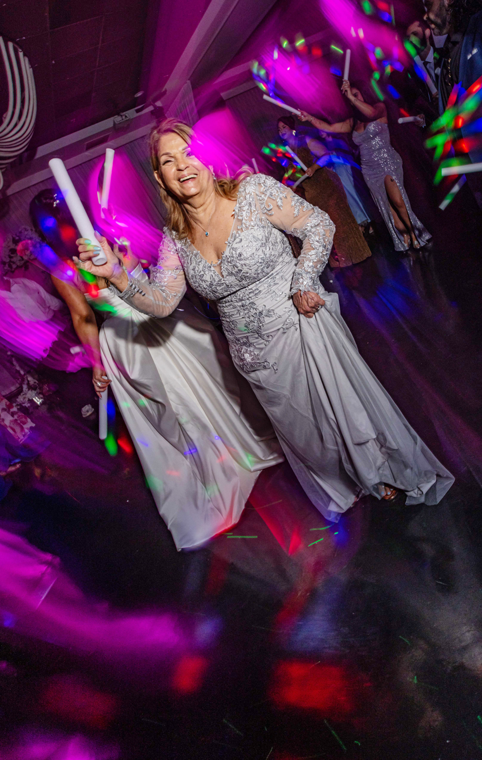 Grandmother in silver gown dancing joyfully during La Hora Loca at Brisas On The Bay, with LED lights and glow sticks by Zeta Event Productions.